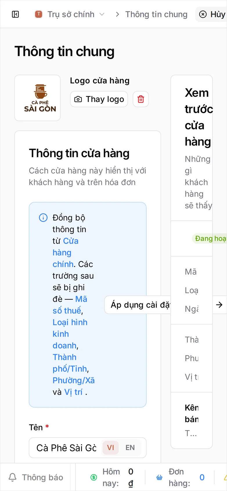 Trang Cài đặt Thông tin chung với nút Hủy bỏ và Lưu ở thanh trên, logo Cà Phê Sài Gòn đã tải lên cạnh nút Thay logo, và thẻ Thông tin cửa hàng bên dưới: khung xanh 'Đồng bộ thông tin từ Cửa hàng chính' kèm nút Áp dụng cài đặt cửa hàng, rồi Tên 'Cà Phê Sài Gòn' ở phía VI của nút chuyển VI/EN, Mã số thuế 0312987656 kèm nút Kiểm tra, Trạng thái Đang hoạt động, cùng hai ô Loại hình kinh doanh và Ngành nghề bị mờ. Các ô bắt buộc đều có dấu sao đỏ
