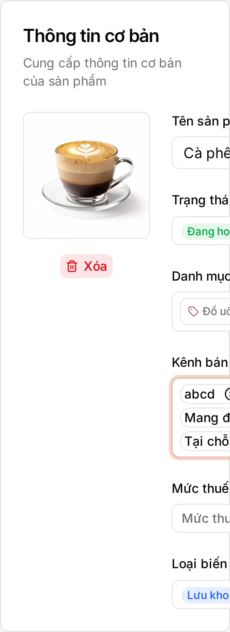 Trang Tạo Sản phẩm: ảnh ly latte đã tải lên cạnh nút Xóa, Tên sản phẩm 'Cà phê Latte' đã nhập ở cả hai tab của nút chuyển VI/EN, đang hiển thị tab EN, Trạng thái Đang hoạt động, Danh mục Đồ uống, ô Kênh bán hiển thị đủ ba kênh Tại chỗ, Mang đi và GrabFood, ô Mức thuế để trống và Loại biến thể Lưu kho. Khung Xem trước trên POS bên phải hiển thị cùng ảnh và tên ở dạng Thiết bị để bàn và Thiết bị di động với giá 0 đ